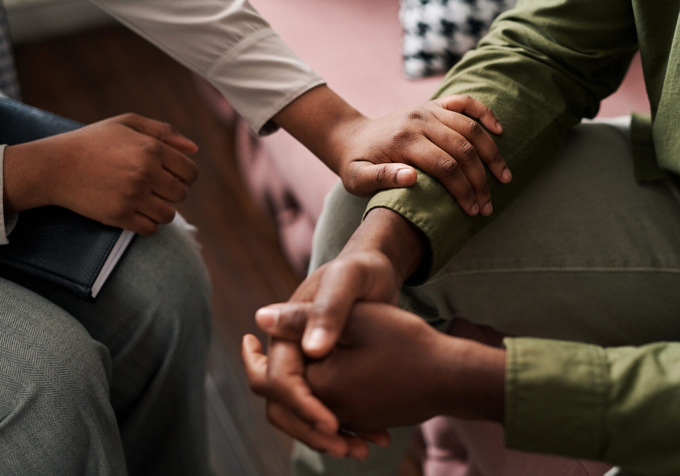 Young African American female psychologist keeping hand of wrist of male patient sitting in front of her and sharing his problems